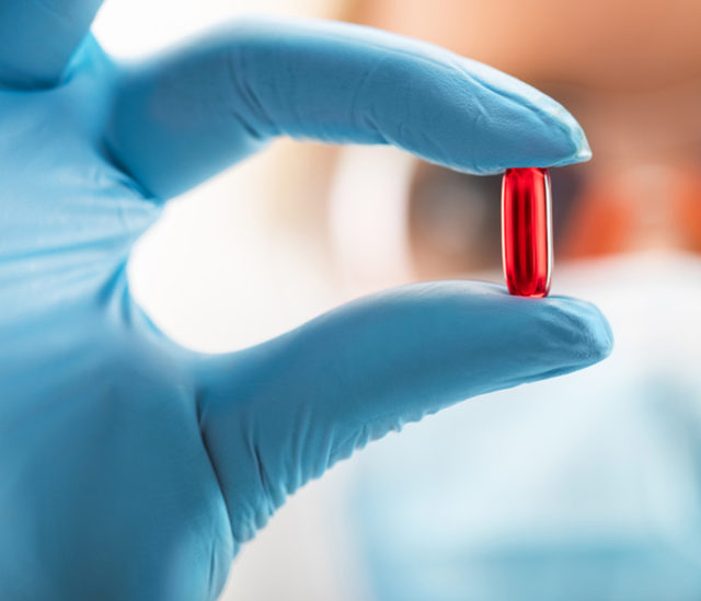 Gélule rouge - médicament tenu par une femme scientifique